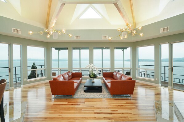 A spacious living room with a large sofa set, a coffee table, and a view of the sea through large windows.