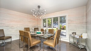 A modern dining area with a glass table, leather chairs, a chandelier, and a view of the outdoors through large windows.
