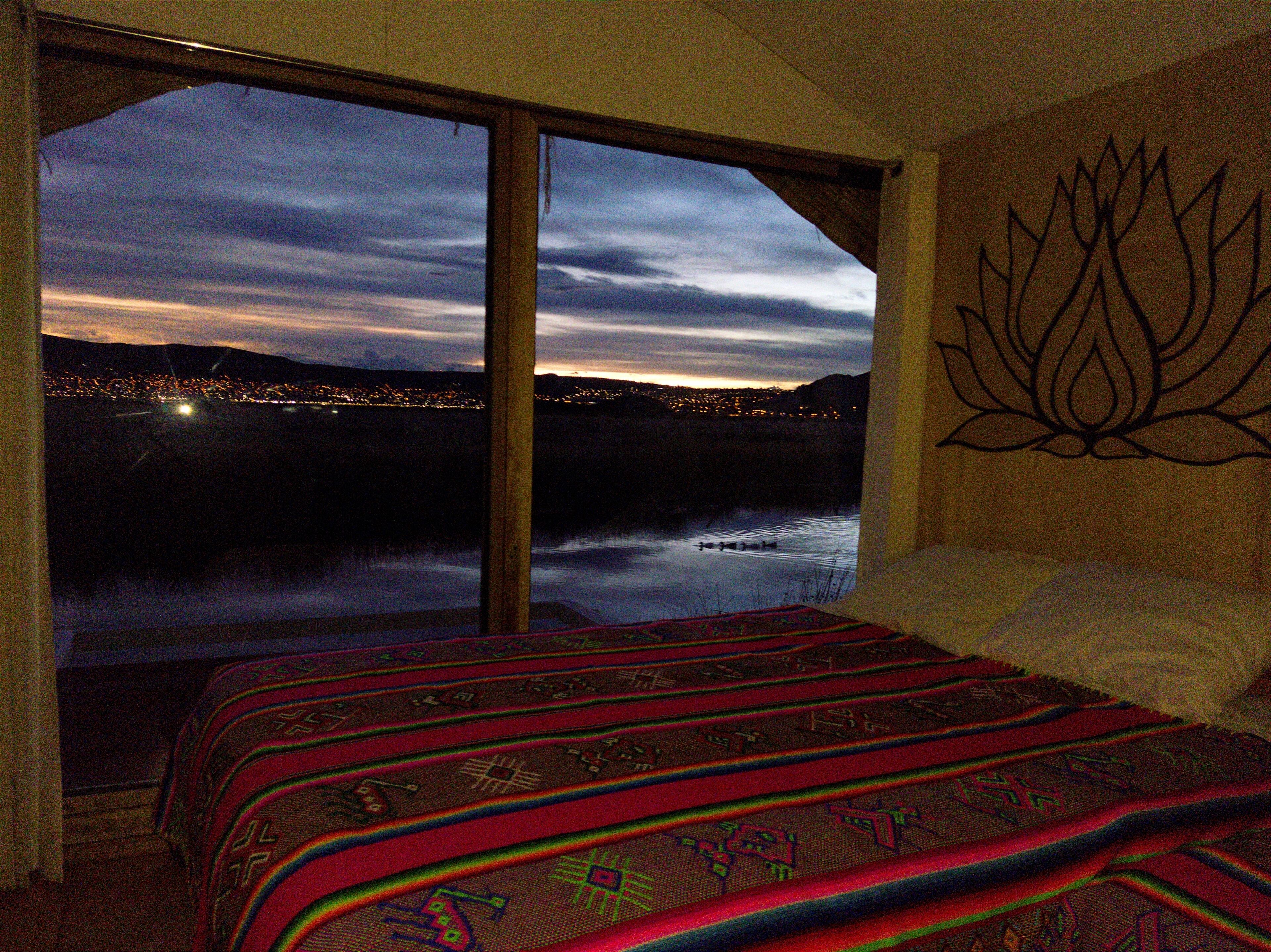 Quarto com uma janela grande que oferece vista para a paisagem urbana ao entardecer.