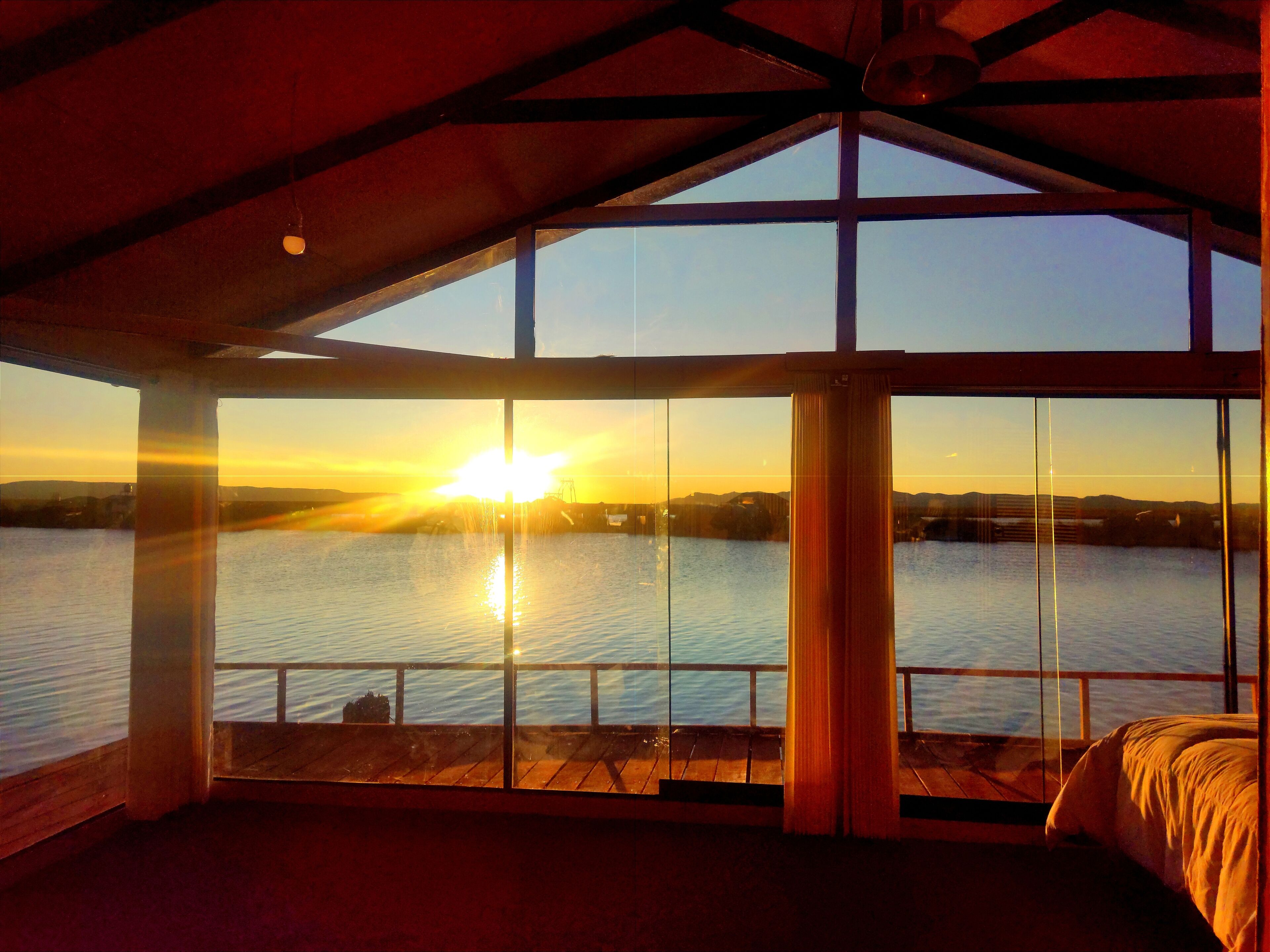 A room with a large window overlooking a body of water at sunset.