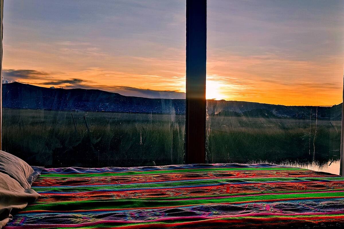A bed with a colorful blanket and a view of a sunset over a body of water and mountains.