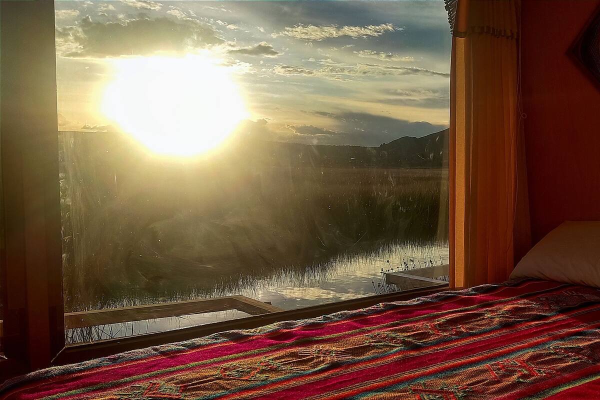 A bedroom with a large window, a bed with a colorful blanket, and a decorative wall piece.