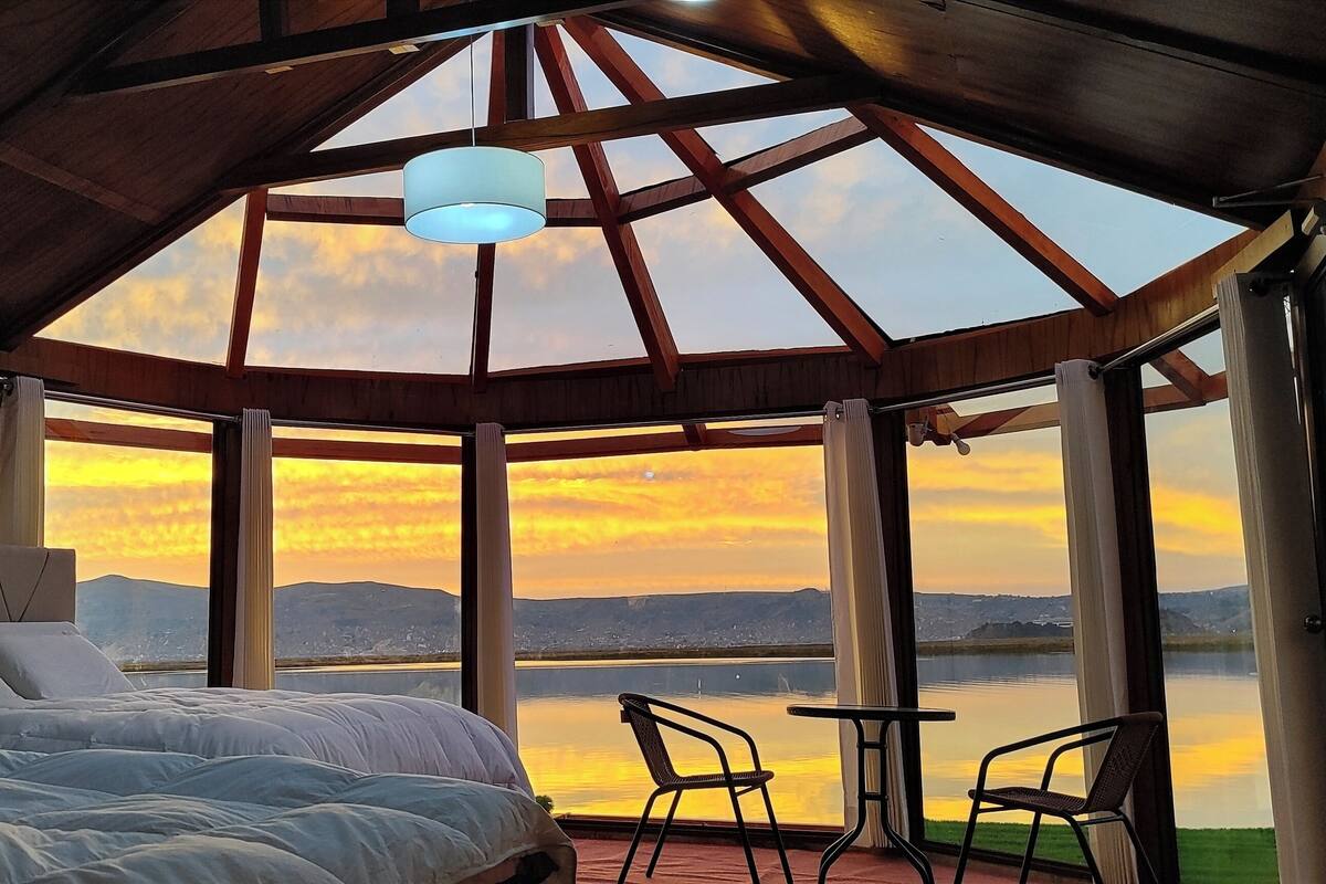 A bedroom with a large bed, a view of a lake, and a table with chairs.