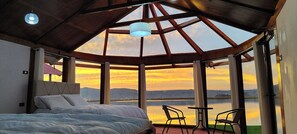 A bedroom with a large bed, a view of a lake, and a table with chairs. - Titicaca Atrion (Puno)