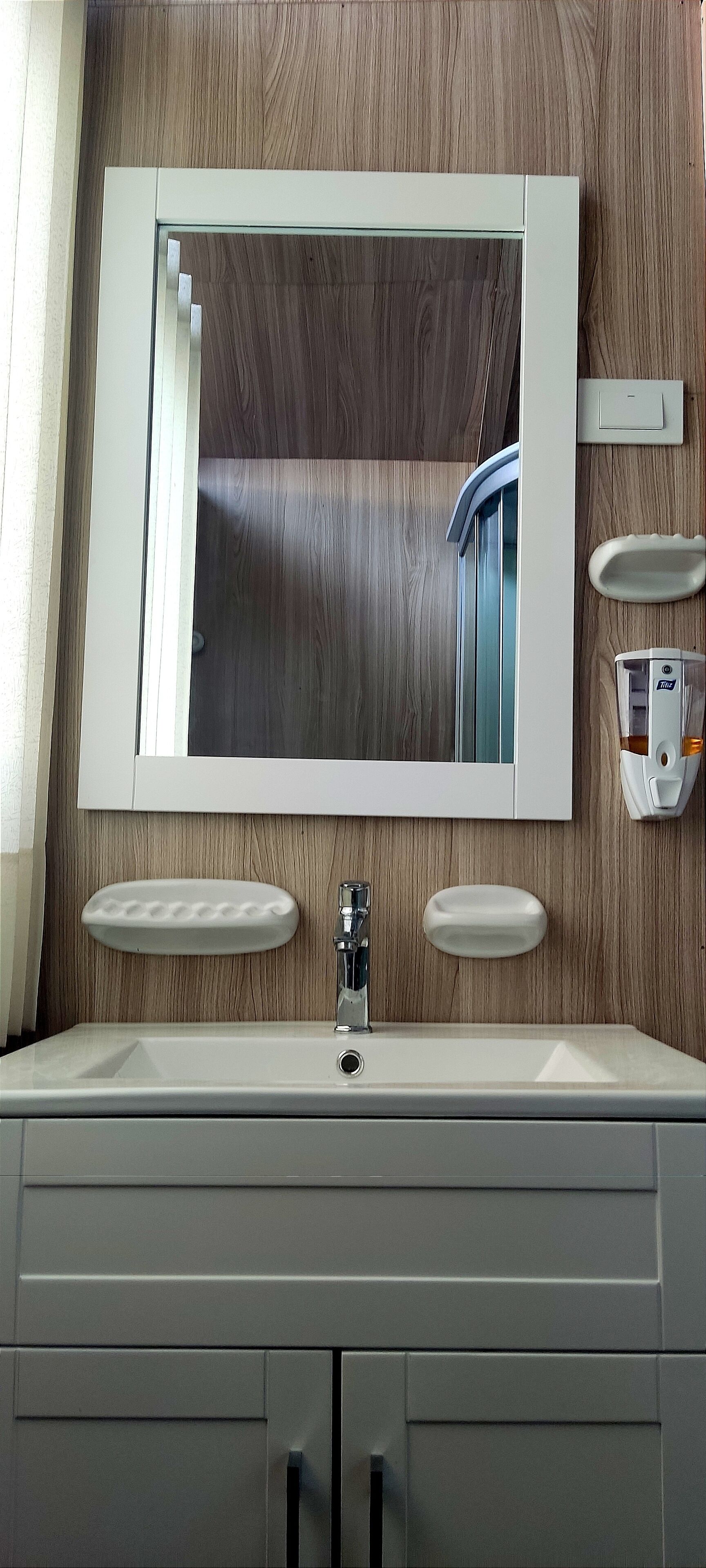 A bathroom with a wooden wall, a large mirror, two sinks, and a soap dispenser.