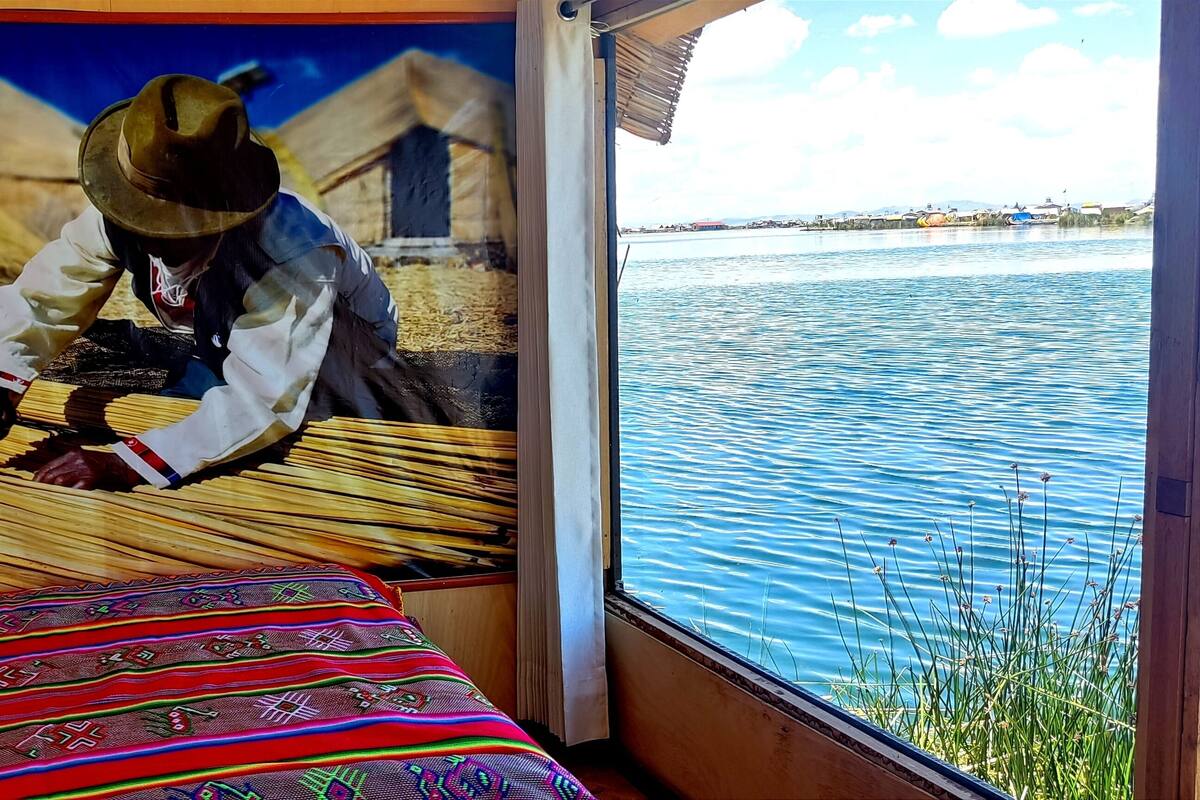 A room with a bed, a mural of a person weaving, and a view of a body of water.