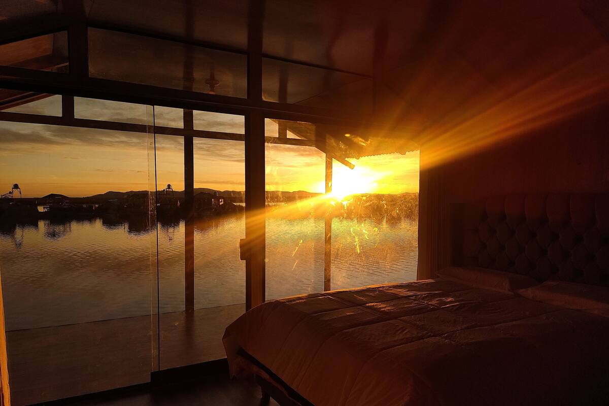 A bedroom with a large window overlooking a body of water and a sunset.
