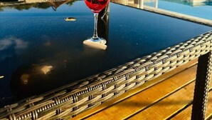 Ein Glas Rotwein auf einem Tisch mit Blick auf einen Pool und grüne Vegetation im Hintergrund.