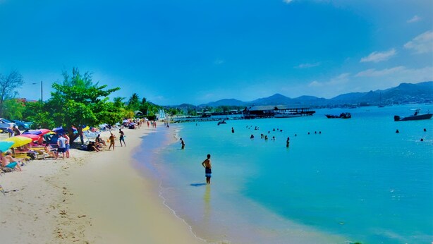 Ein Strand mit klarem türkisblauem Wasser, Menschen beim Schwimmen und Sonnenschirmen im Sand.