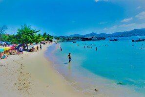 A beach with clear turquoise water, people swimming, and umbrellas on the sand.