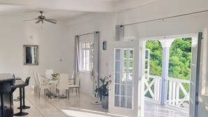 Ein geräumiger Raum mit Essbereich, Deckenventilator und Blick auf Grün hinter großen Fenstern.