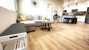 Ein modernes Wohnzimmer mit grauem Sofa, Couchtisch und Küchenbereich mit weißen Schränken und einem Edelstahlkühlschrank.