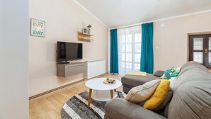 Un salon moderne avec un téléviseur à écran plat, un canapé, une table basse et une fenêtre avec des rideaux.