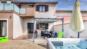 Une maison moderne dotée d’un patio comprenant un jacuzzi, du mobilier d’extérieur et un espace salon abrité.