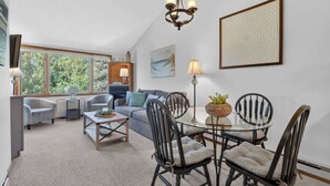 A cozy living room with a fireplace, a dining table with chairs, and a large window with a view of trees. - Ephraim Condo | Walk to Water, Wilson's and Shops (Ephraim)