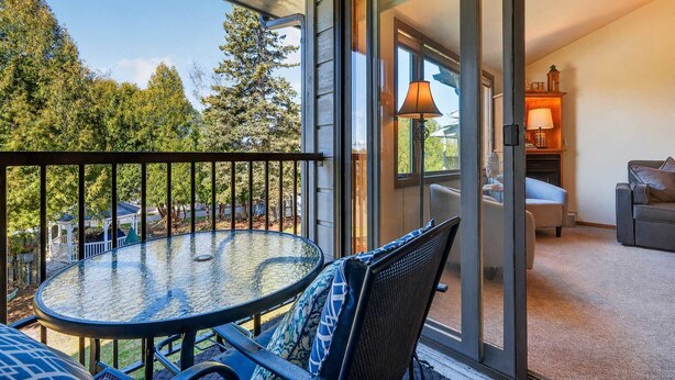 A balcony with a glass door, a round table with chairs, a sofa, and a lamp. - Ephraim Condo | Walk to Water, Wilson's and Shops (Ephraim)