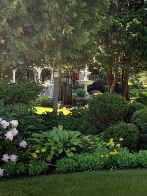 Un jardin avec une fontaine, différentes plantes et une clôture blanche.