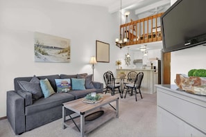 A living room with a grey sofa, a wooden coffee table, and a dining area with chairs and a small island.
