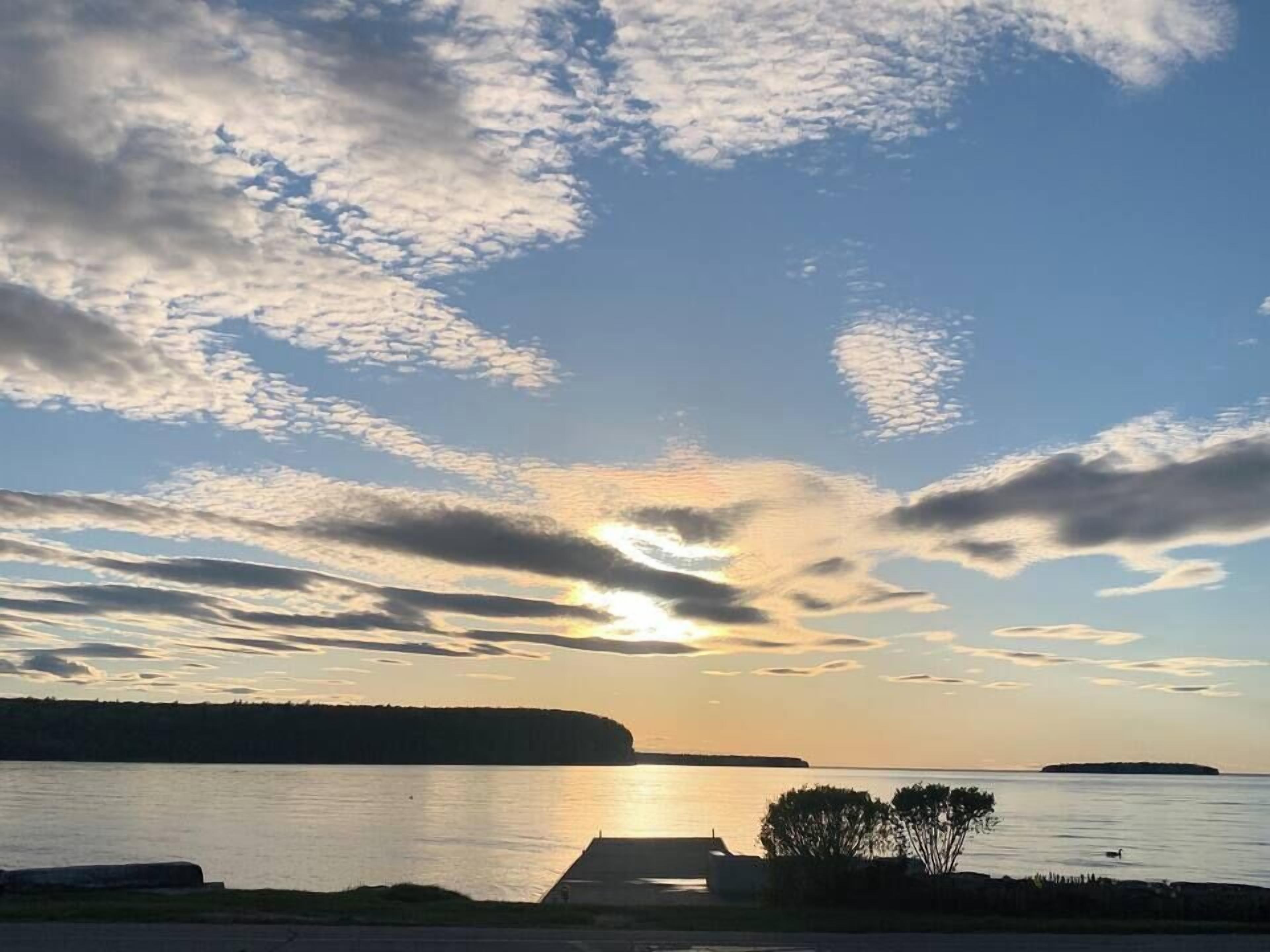 Atardecer sobre un cuerpo de agua tranquilo, con un muelle y árboles en primer plano.