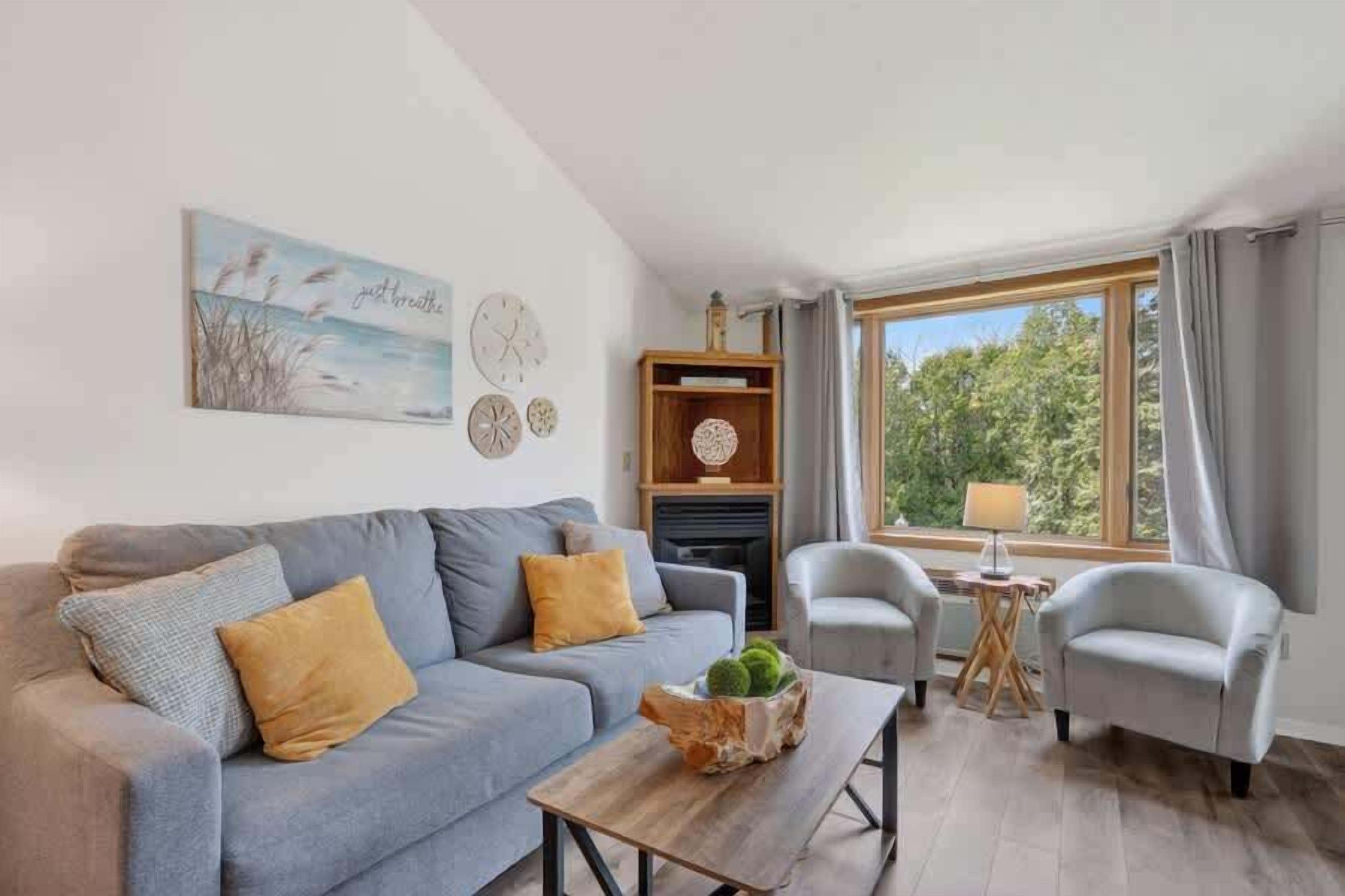 A living room with a sofa, two armchairs, a coffee table, a fireplace, and a large window with curtains.