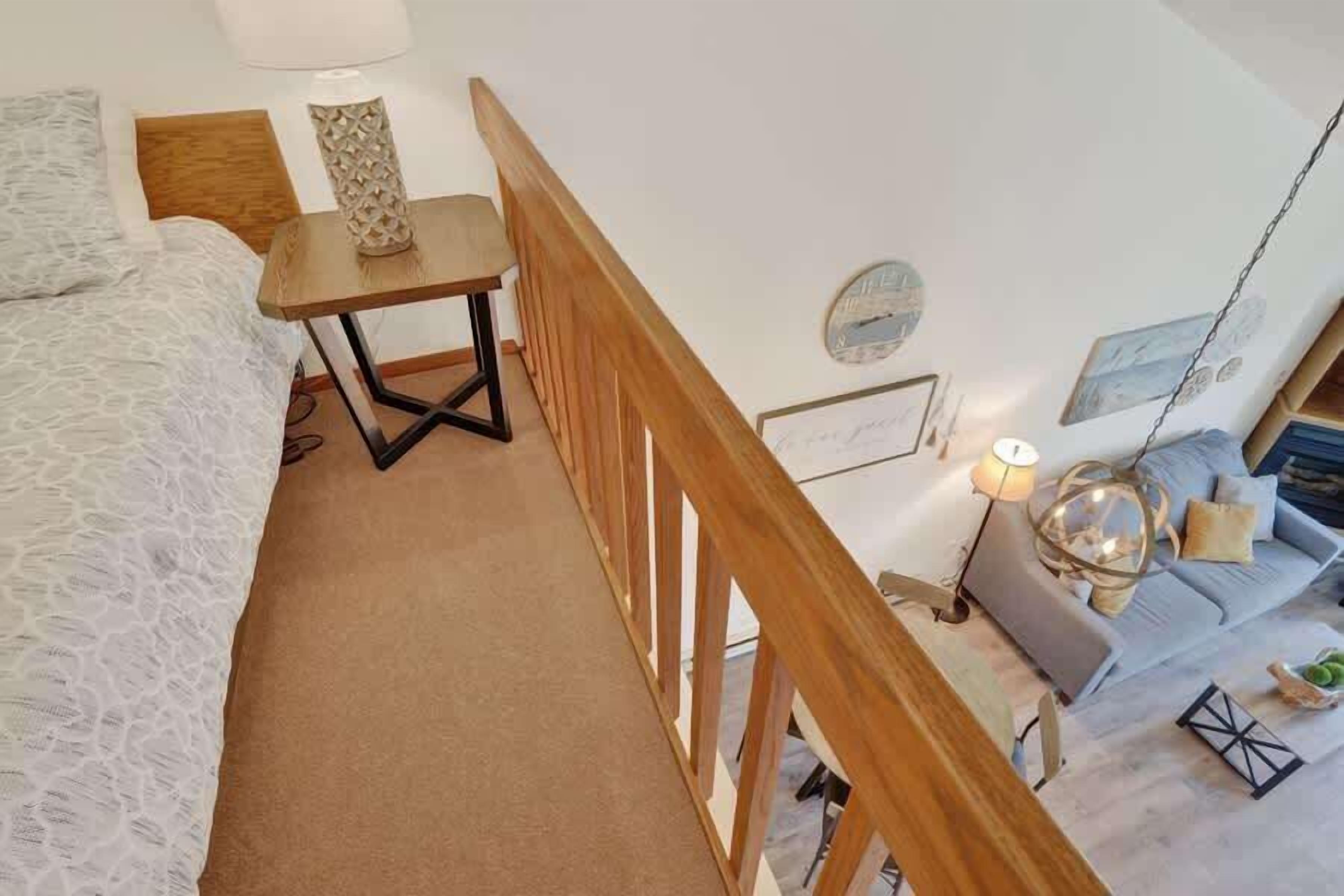 A bedroom with a bed, a wooden table, a hanging light fixture, and a view of the living area.