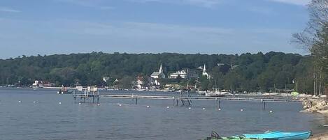 A calm waterfront with a boat on the shore, a pier extending into the water, and a building with a steeple in the background.