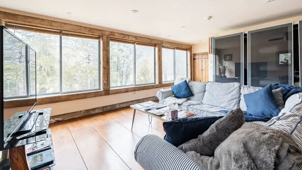 A spacious living room with large windows, a sofa, a coffee table, and a television.