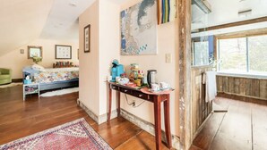 A spacious living room with a wooden floor, a large window, and a cozy seating area with a sofa and a chair.