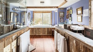 A bathroom with a wooden vanity, a large bathtub, and a window providing a view of the outdoors.