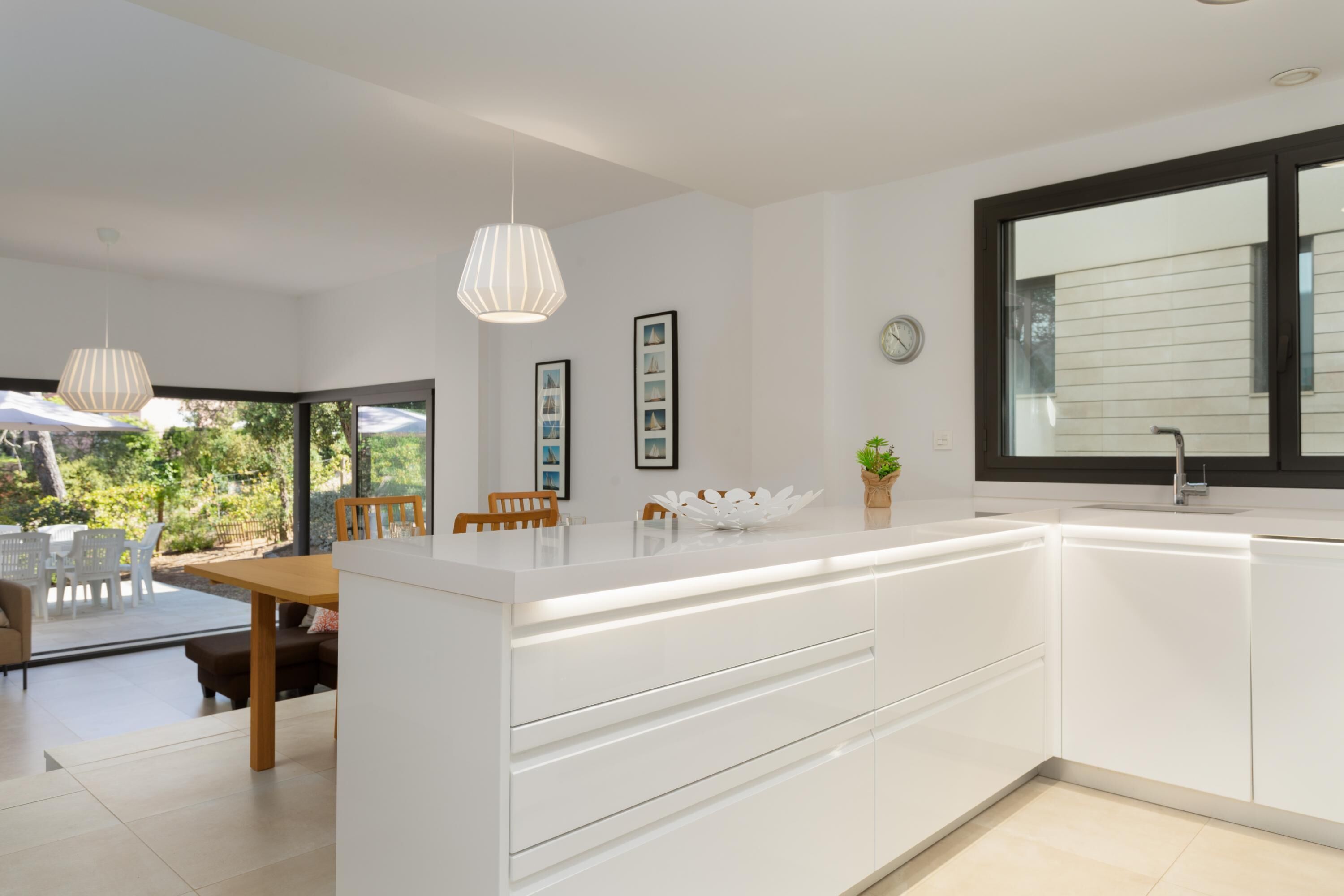 A modern kitchen with white cabinetry, a large island, pendant lighting, and a view of the outdoors.