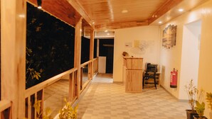 A hotel corridor with wooden flooring, a wooden reception desk, a fire extinguisher, and potted plants.