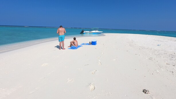 A beach with a clear sky, a boat, and footprints on the sand.