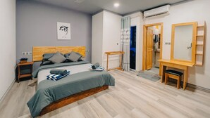 A bedroom with a bed, a ceiling fan, an air conditioning unit, a wooden headboard, a bedside table, a mirror, and a door leading to another room.