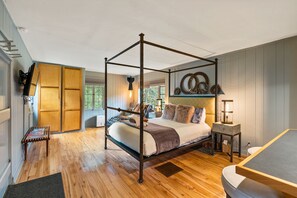 Una cama con dosel y estructura de madera, una mesita de noche con lámpara y vistas al exterior a través de una ventana.