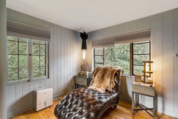 Un dormitorio con cama, calefactor, lámpara y ventana con vistas a árboles.