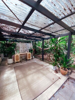 A covered patio area with a concrete floor, a wooden table, and several potted plants. - Sanctuary Studio (The Pocket)