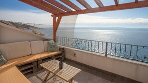Um deck de madeira com um banco acolchoado e uma mesa, com vista para um corpo de água sob um céu claro.