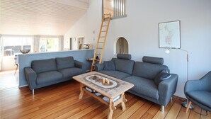 Una sala de estar moderna con piso de madera, sofás grises, una mesa de centro de madera y una escalera que da a un altillo.