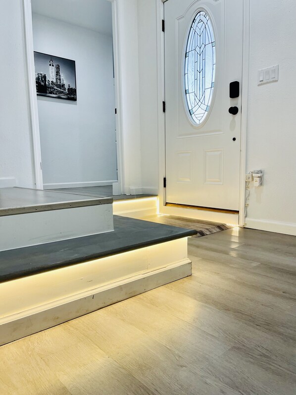 A modern entryway with a wooden floor, a white door with a glass window, and a small step leading to the door.