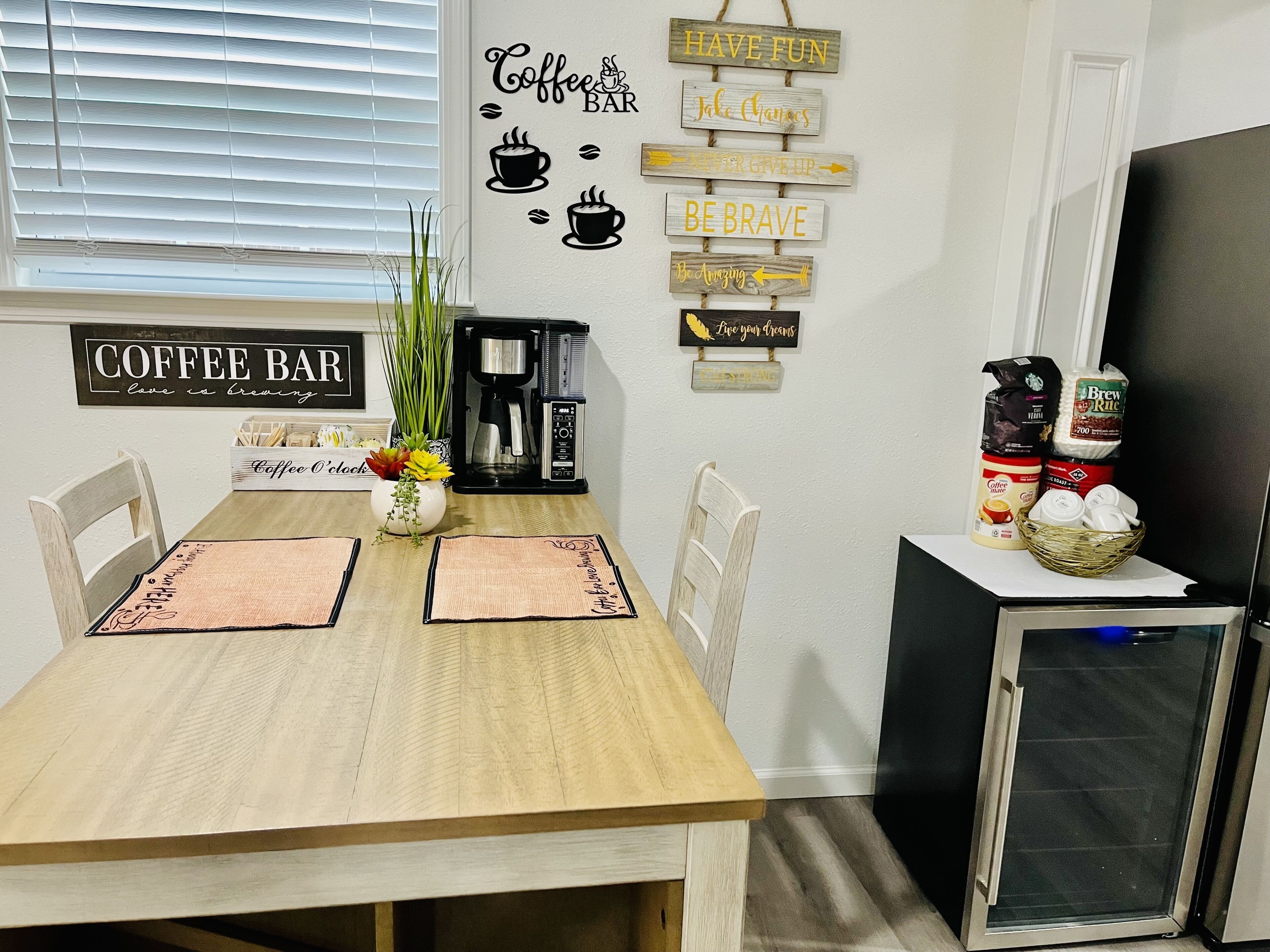 A dining area with a wooden table, chairs, a coffee station, and motivational wall art.