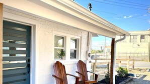 Una casa con puerta de garaje, dos sillas de madera afuera, felpudo y vista despejada a la calle y edificios vecinos.