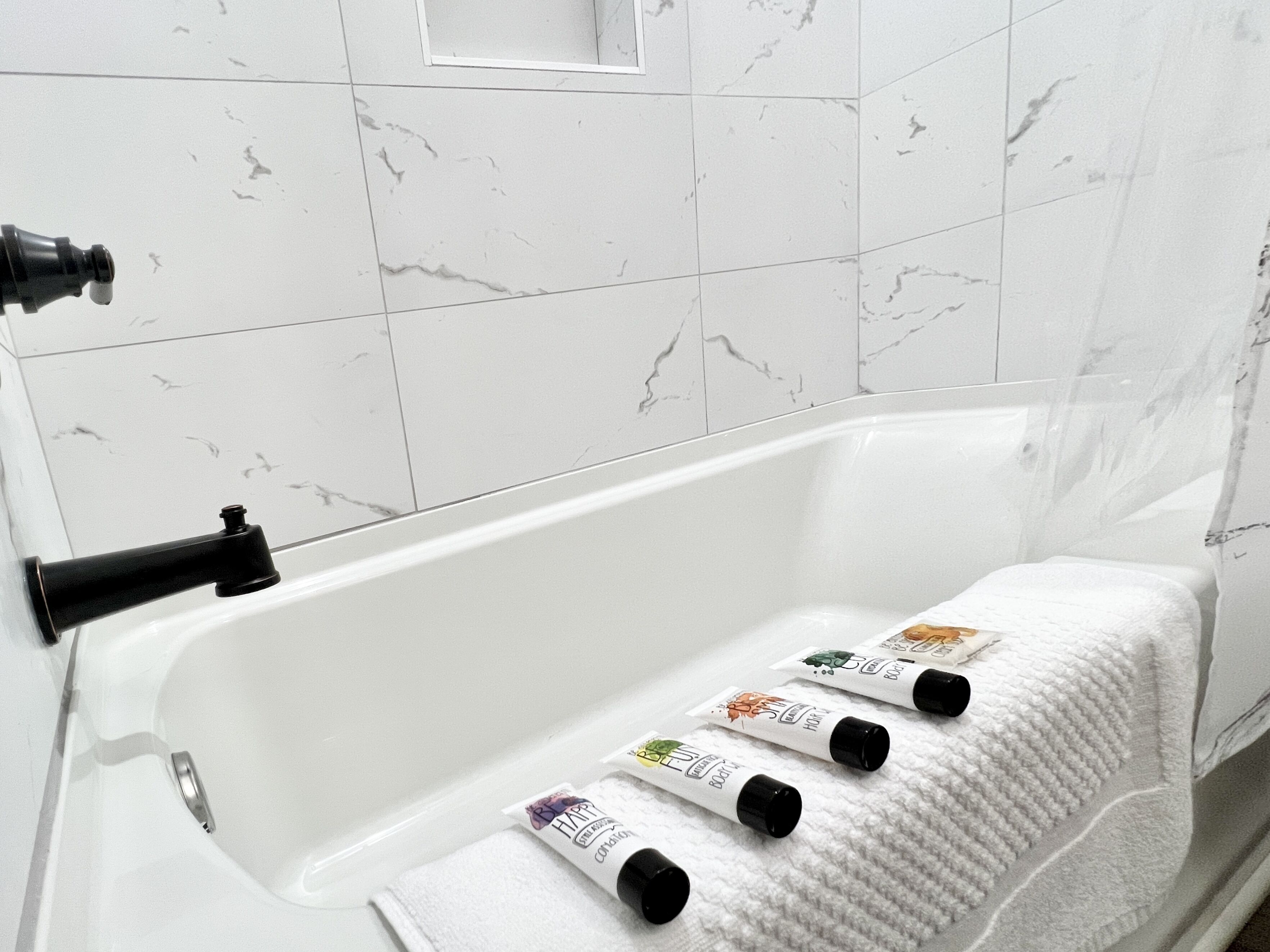 Ein Badezimmer mit einer weißen Badewanne, einem Handtuch und vier Haarpflegeprodukten am Rand.
