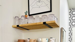 Una cocina con estantes de madera que sostienen cristalería y tazas, una cafetera y un cuadro enmarcado en la parte superior.