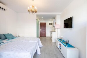 A bedroom with a bed, a bedside table with a lamp, a TV mounted on the wall, and a door leading to a bathroom. - RENTHAS Studio in Benalmádena (Benalmadena)