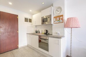 A compact kitchen with white cabinets, a microwave, an oven, and a wooden door. - RENTHAS Studio in Benalmádena (Benalmadena)