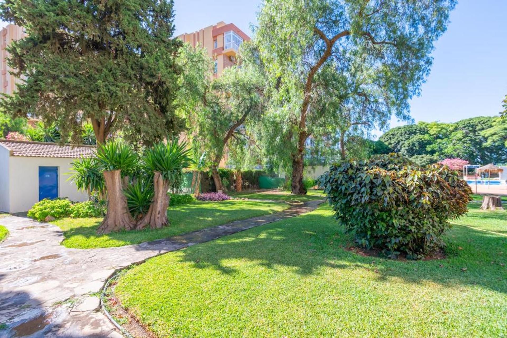 A well-maintained garden with a pathway, trees, and a small building with a blue door.