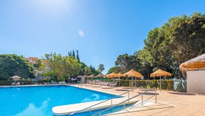 A swimming pool with a tiled deck, lounge chairs, and thatched umbrellas. - RENTAS Benalmádena Beach Studio (Benalmadena)