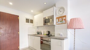 A modern kitchen with white cabinets, stainless steel appliances, a wooden door, and a clock on the wall. - RENTAS Benalmádena Beach Studio (Benalmadena)
