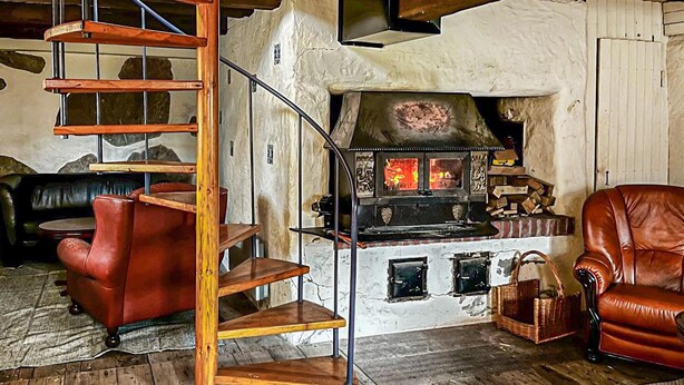 A rustic interior with a wooden spiral staircase, a stone fireplace, leather sofas, and a rustic wooden floor. - Nice home in Agunnaryd with kitchen (Agunnaryd)