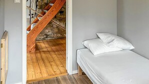 A bedroom with a wooden staircase leading to a stone wall, a bed with white bedding, and wooden flooring. - Nice home in Agunnaryd with kitchen (Agunnaryd)